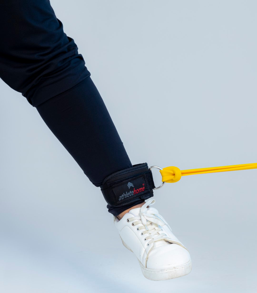 Ankle strap with a yellow hook attached to a shoe, securing an exercise band or cable to the ankle for resistance training.