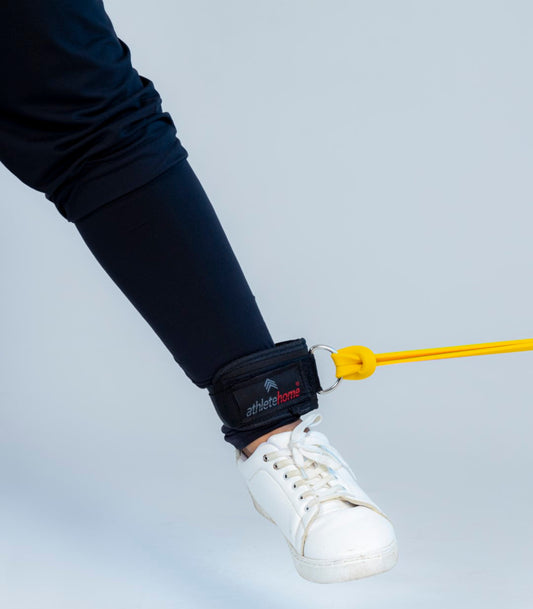 Ankle strap with a yellow hook attached to a shoe, securing an exercise band or cable to the ankle for resistance training.